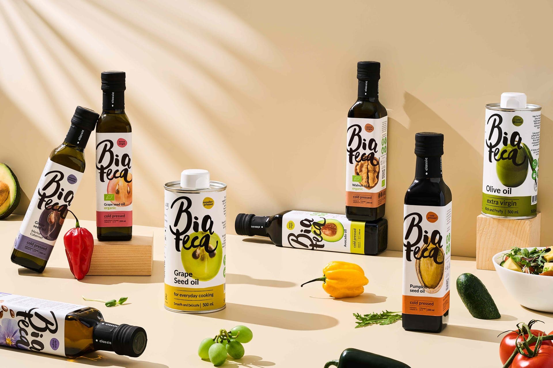 Biateca oil collection featuring glass bottles and tin containers with fresh ingredients including peppers, avocado, tomatoes, and herbs